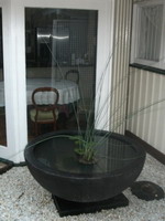 large garden water bowl on base, black volcanic scoria finish, in private courtyard with white stone landscaping